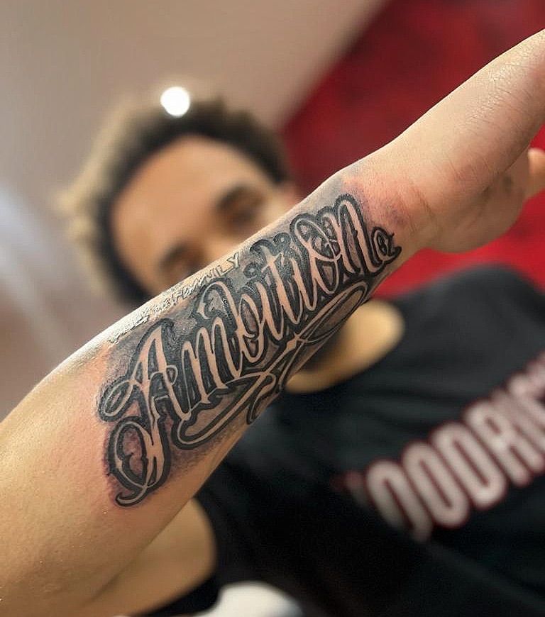 Custom script tattoo reading Ambition on a client's forearm